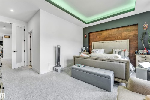 Recessed ceiling with perimeter lighting, accent wall featuring horizontal wood paneling, wall-mounted light fixtures, white paneled doors with black hardware, and light-toned carpeting - 208 33 Street, Edmonton, AB 