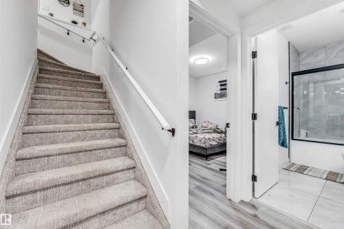 Carpeted staircase with white handrail, featuring a nearby bedroom with wood-finish flooring and a bathroom with a glass-enclosed tub/shower and large format tile flooring - 208 33 Street, Edmonton, AB 