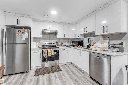Well-appointed kitchen featuring white cabinetry, stainless steel appliances, light-toned countertops, tile backsplash, and wood-finish flooring - 208 33 Street, Edmonton, AB 