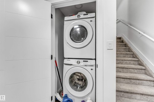 Dedicated laundry closet featuring a stackable washer and dryer, adjacent to a carpeted staircase with a white handrail - 208 33 Street, Edmonton, AB 