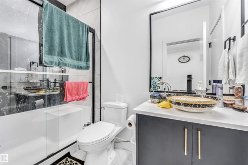 Bathroom featuring a vessel sink, dark vanity with gold-tone pulls, a framed mirror, and a glass-enclosed shower with black-veined wall tile - 208 33 Street, Edmonton, AB 