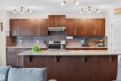 Kitchen featuring dark wood-finish cabinetry with brushed nickel hardware, light granite countertops, and a modern stainless steel range with overhead microwave - 74 Santana Crescent, Fort Saskatchewan, AB 