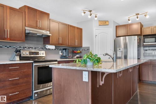 Spacious kitchen featuring an island with a built-in sink and faucet, wood-finish cabinetry, stainless steel appliances, and track lighting - 74 Santana Crescent, Fort Saskatchewan, AB 