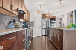 Modern kitchen featuring wood-finish cabinetry, granite-style countertops, stainless steel appliances, a tiled backsplash, and dark wood-finish flooring - 
