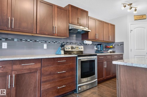 Kitchen featuring rich wood cabinetry, light-toned countertops, a stainless steel range, and a gray subway tile backsplash with decorative accent banding - 74 Santana Crescent, Fort Saskatchewan, AB 