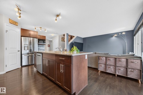 Kitchen island with a granite-style countertop, stainless steel appliances, dark wood-finish cabinetry, and wood-finish flooring - 74 Santana Crescent, Fort Saskatchewan, AB 
