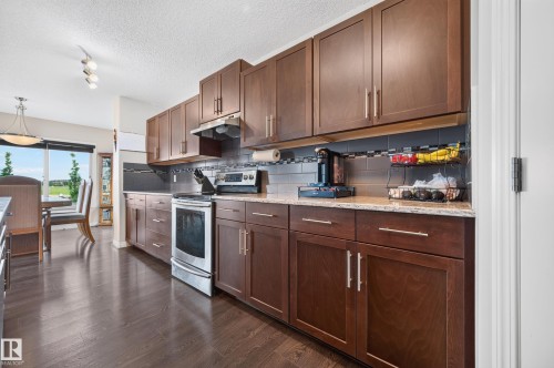Kitchen featuring dark wood cabinetry, light-toned countertops, a stainless steel electric range, and a tiled backsplash - 74 Santana Crescent, Fort Saskatchewan, AB 