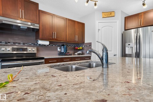 Kitchen featuring a double basin stainless steel sink with a high-arc faucet, granite countertops, and rich wood cabinetry - 74 Santana Crescent, Fort Saskatchewan, AB 