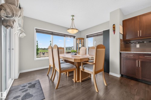 Dining area featuring wood-finish flooring, a contemporary pendant light fixture, and large windows with roller blinds - 74 Santana Crescent, Fort Saskatchewan, AB 