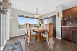 Dining area featuring wood-finish flooring, a contemporary pendant light fixture, and large windows with roller blinds - 