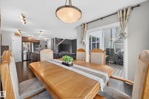 Open concept main level featuring a dining area with wood-finish flooring, a sliding glass door to the outdoor deck, and a contemporary ceiling light fixture - 74 Santana Crescent, Fort Saskatchewan, AB 