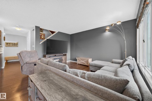 Living room featuring wood-finish flooring, a wall-mounted television, and built-in shelving - 74 Santana Crescent, Fort Saskatchewan, AB 