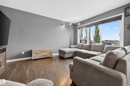 Living area featuring wood-finish flooring, a large picture window, and neutral wall tones - 74 Santana Crescent, Fort Saskatchewan, AB 