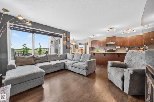Open-concept living area featuring wood-finish flooring and a kitchen with warm wood cabinetry - 74 Santana Crescent, Fort Saskatchewan, AB 
