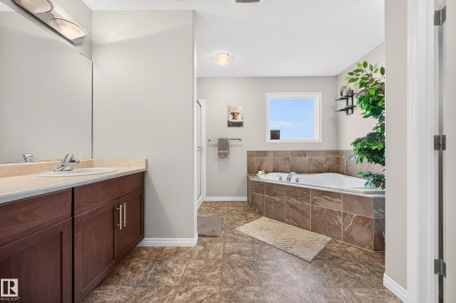 Bathroom featuring a corner soaking tub with tiled surround, a separate glass-enclosed shower, and a vanity with a light-colored countertop and integrated sink - 74 Santana Crescent, Fort Saskatchewan, AB 
