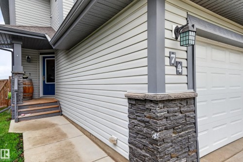 Exterior featuring horizontal siding, stone veneer accents, a covered entry, a paneled garage door, and a blue entry door - 74 Santana Crescent, Fort Saskatchewan, AB 