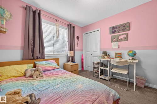 Bedroom featuring wall-to-wall carpeting, a window with horizontal blinds and drapes, a built-in closet with bifold doors, a wood-finish headboard, and a two-tone painted wall - 74 Santana Crescent, Fort Saskatchewan, AB 