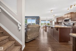Open-concept living space featuring wood-finish flooring, a kitchen island with seating, dark wood cabinetry, a tile backsplash, and stainless steel appliances - 