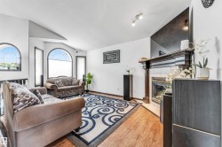Living area featuring wood-finish flooring, a fireplace with a decorative mantel, and arched windows - 