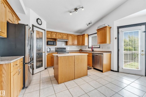 Kitchen featuring wood cabinetry, stainless steel appliances, a central island, tile flooring, and a vaulted ceiling with track lighting - 6719 164 Ave, Edmonton, AB 