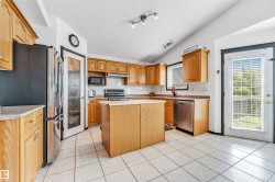 Kitchen featuring wood cabinetry, stainless steel appliances, a central island, tile flooring, and a vaulted ceiling with track lighting - 