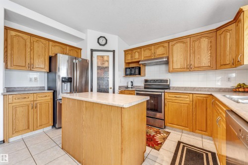 Kitchen featuring wood cabinetry, stainless steel appliances, a center island with countertop, and ceramic tile flooring - 6719 164 Ave, Edmonton, AB 