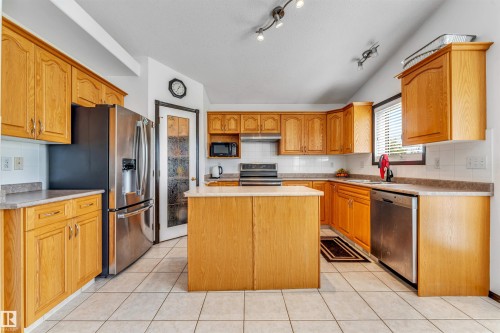 Spacious kitchen featuring light wood cabinetry, a central island, and white tile flooring - 6719 164 Ave, Edmonton, AB 