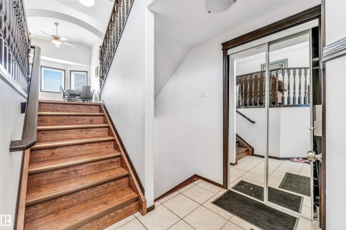 Entryway featuring a wood-finish staircase with dark wood railings, leading to a vaulted ceiling with an overhead light fixture - 6719 164 Ave, Edmonton, AB 