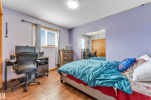 Bedroom with wood-finish flooring, a double window featuring blinds, a built-in closet with bifold doors, and a flush mount ceiling light - 6719 164 Ave, Edmonton, AB 