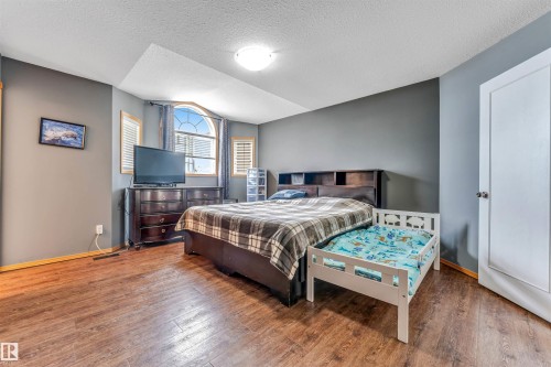 Bedroom featuring a prominent arched window, wood-finish flooring, a contemporary ceiling light fixture, neutral gray walls, and white trim - 6719 164 Ave, Edmonton, AB 