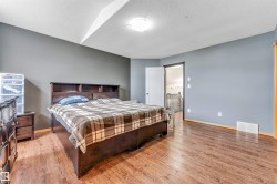 Spacious room featuring wood-finish flooring, neutral gray walls, a ceiling-mounted light fixture, and a white door leading to a hallway with a wooden railing - 