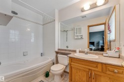 Bathroom featuring a built-in bathtub with white tile surround, a wood-finish vanity with an integrated sink, a large wall-mounted mirror, and overhead vanity lighting - 