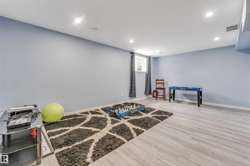 Lower level recreation room featuring light blue walls, recessed ceiling lighting, a window with dark curtains, and light wood-finish flooring - 6719 164 Ave, Edmonton, AB 