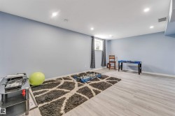 Lower level recreation room featuring light blue walls, recessed ceiling lighting, a window with dark curtains, and light wood-finish flooring - 