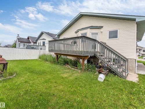 Rear exterior featuring an elevated wood deck with stairs, beige vinyl siding, and a white chain-link fence - 6719 164 Ave, Edmonton, AB 