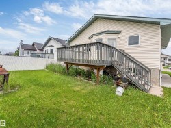 Rear exterior featuring an elevated wood deck with stairs, beige vinyl siding, and a white chain-link fence - 