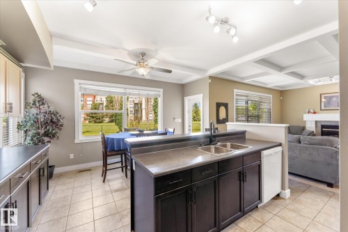 Open-concept kitchen featuring an island with double sink, dark wood-finish cabinetry, tile flooring, and a dining area with a large window - 488 Macewan Road, Edmonton, AB 