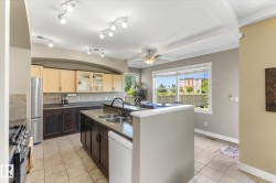 Spacious kitchen featuring an expansive island with dual basin sink, light and dark wood-finish cabinetry, tile flooring, and track lighting - 