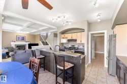 Open-concept living space featuring a coffered ceiling, a contemporary gas fireplace with a mantel, and a kitchen island with seating - 