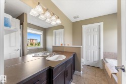 Bathroom featuring a double vanity with dark wood-finish cabinetry and integrated sinks, a wide window above a built-in tub with stone-finish tile surround, and neutral-toned wall paint - 