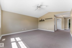 Spacious room featuring vaulted ceilings, a ceiling fan with integrated lighting, carpeted flooring, and neutral wall tones - 