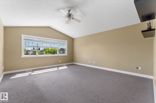 Spacious room featuring vaulted ceilings, a large multi-pane window, neutral wall tones, and gray patterned carpeting - 488 Macewan Road, Edmonton, AB 