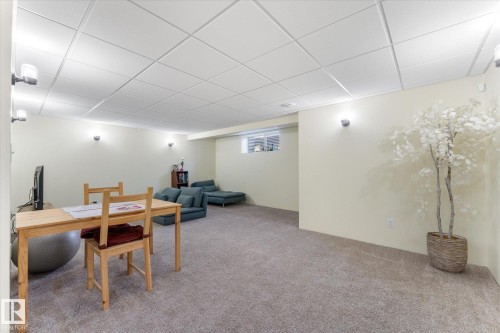 Spacious carpeted room featuring a drop ceiling with integrated lighting, multiple wall sconces, and a high-set window - 488 Macewan Road, Edmonton, AB 