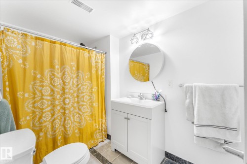 Full bathroom featuring a white vanity with integrated sink, chrome hardware, a round wall-mounted mirror, and tile flooring - 488 Macewan Road, Edmonton, AB 