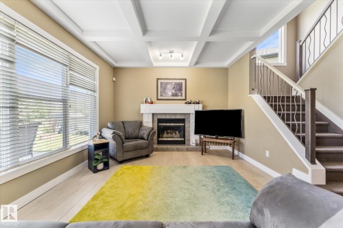 Living area featuring wood-finish flooring, a white coffered ceiling, and a fireplace with a stone surround and white mantel - 488 Macewan Road, Edmonton, AB 