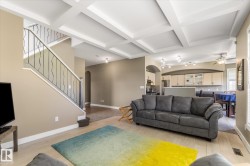 Living space featuring a coffered ceiling, wood-finish flooring, and a staircase with wrought iron balusters - 