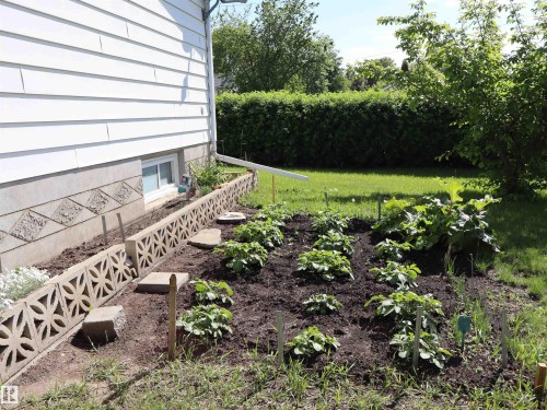 Cultivated garden area featuring established plantings, decorative concrete block edging, and a foundation window - 5530 46 Street, Barrhead, AB 