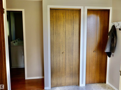 Wood-finish bi-fold closet doors with round knobs, white trim, and a patterned floor tile - 5530 46 Street, Barrhead, AB 