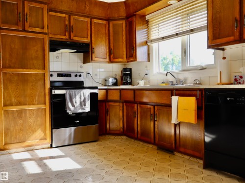 Kitchen featuring wood cabinetry, white tile backsplash, a stainless steel range, and a dual-basin sink under a window - 5530 46 Street, Barrhead, AB 