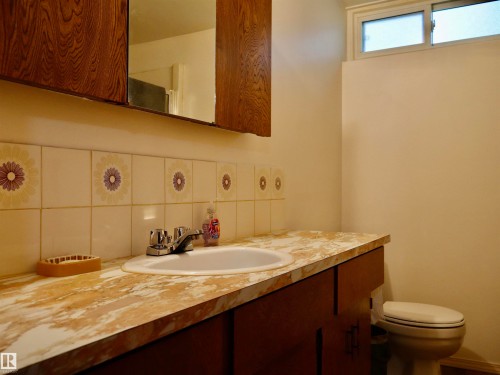 Bathroom vanity featuring a drop-in sink, chrome faucet, and patterned tile backsplash - 5530 46 Street, Barrhead, AB 